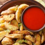 Garlic Parmesan potato wedges served with marinara dipping sauce on a rustic plate.