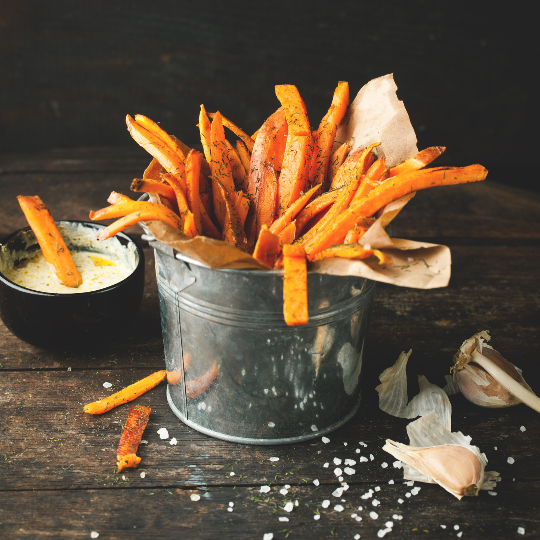 Crispy oven-baked sweet potato fries seasoned with rosemary and garlic, served in a metal bucket with a creamy dipping sauce.
